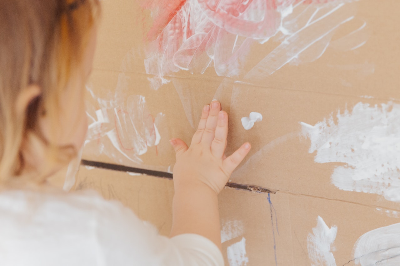 child painting with white paint at home on cardboard