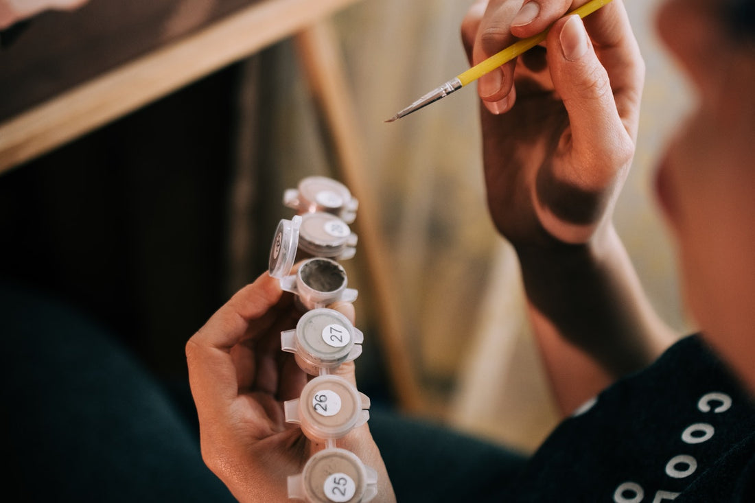 woman holding paint by number paints with paintbrush for painting at home