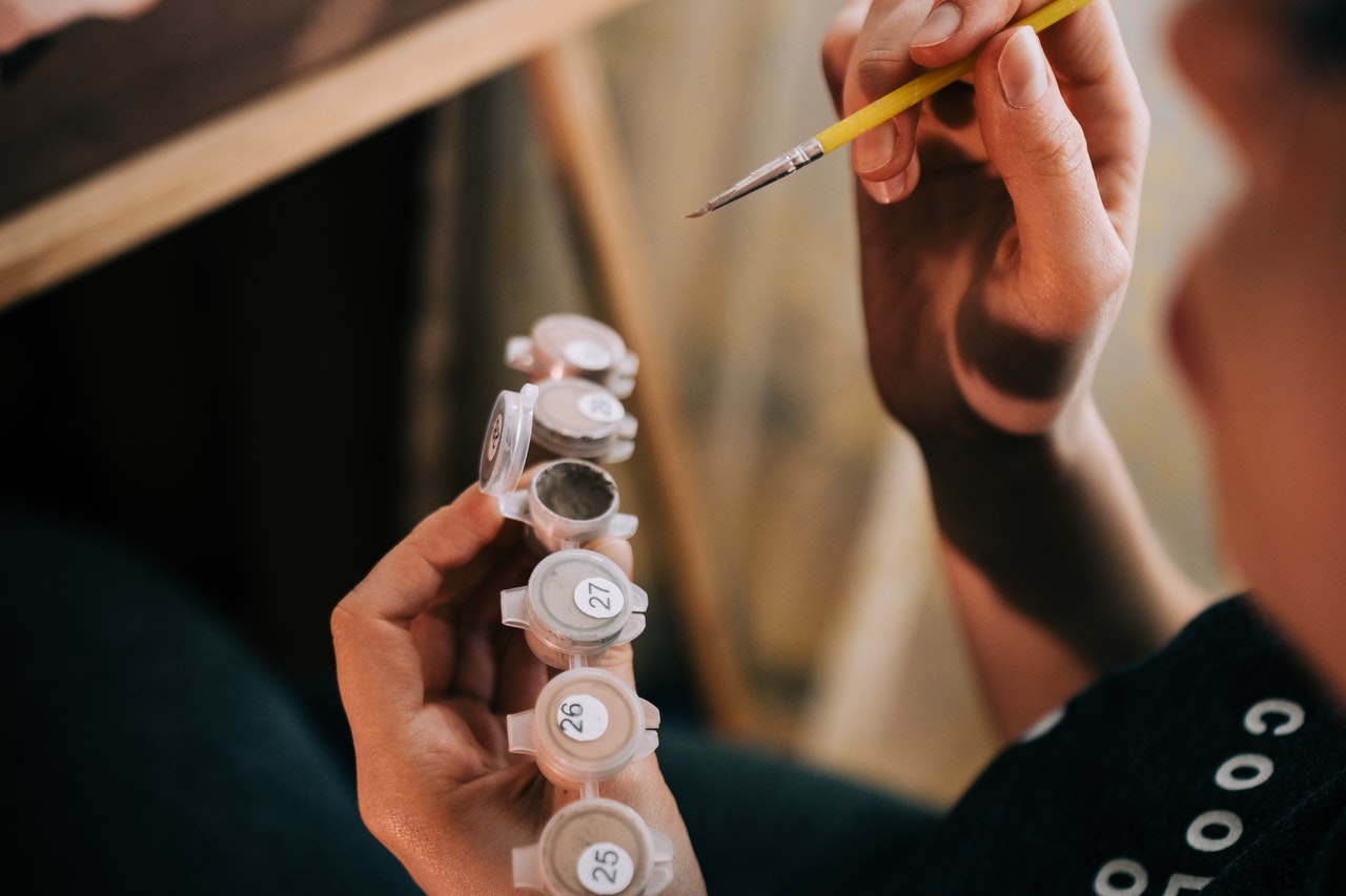 woman holding paint by number paints with paintbrush for painting at home